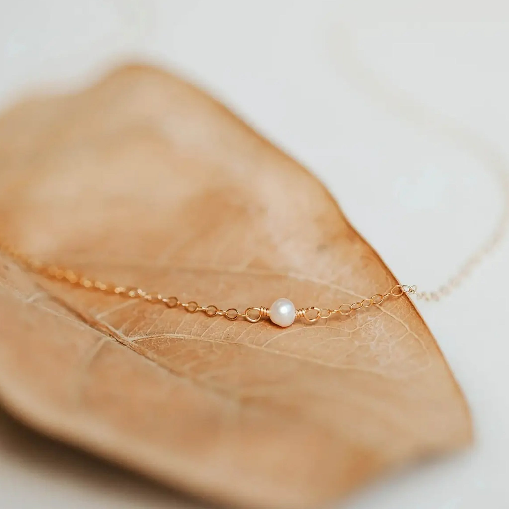 A gold chain necklace with a freshwater pearl in the center. 