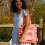 A red and white gingham printed tote bag with shoulder straps and a ruffle edge detail. 