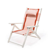 A pink and white folding beach chair with dark pink / reddish accents, a head support pillow and a zip pocket on the back of the chair.