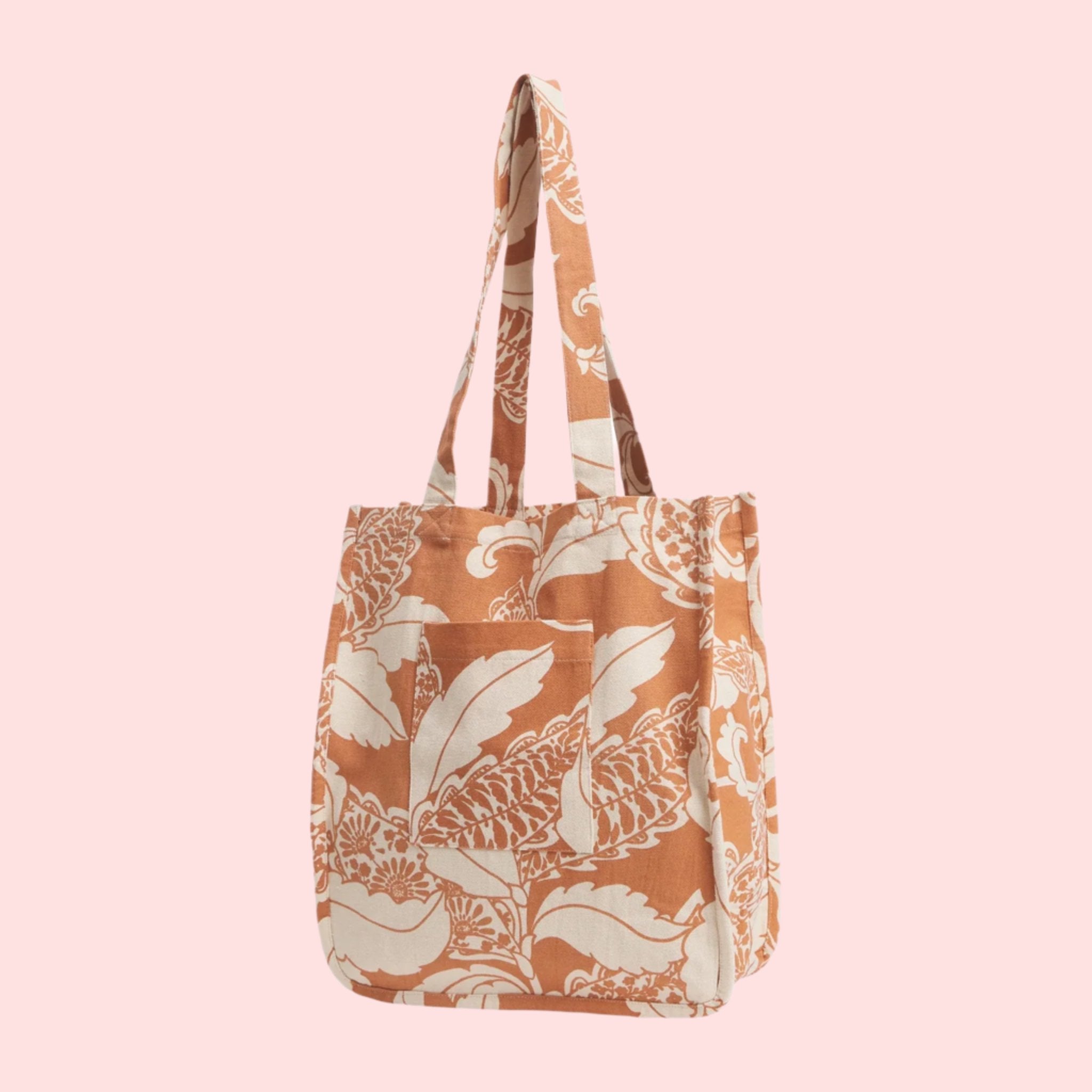 A tan and white canvas tote bag with a front pocket and a paisley pattern. 