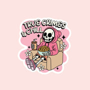 A pink decorative sticker with a graphic of a skeleton eating popcorn in a comfy pink hoodie and text above that reads, "True Crimes & Chill". 