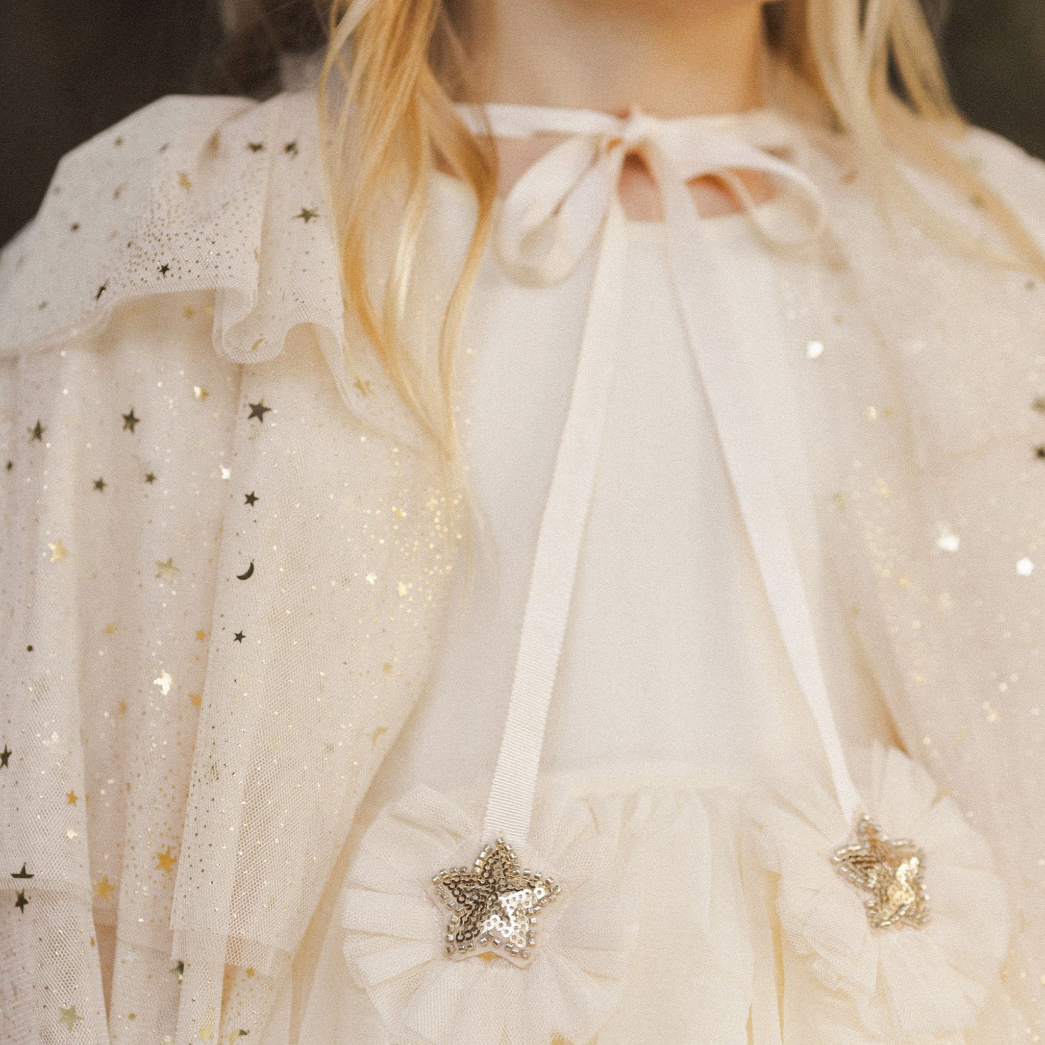 A champagne colored tulle cape with layered tiers and a neck tie with two star ribbons.