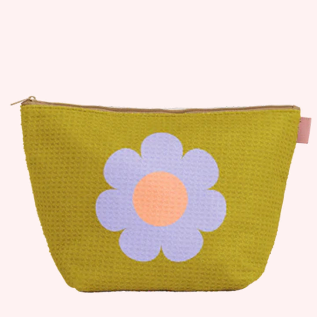 On a light pink background is a chartreuse green tote with a subtle waffle knit texture and a purple daisy graphic in the center. 