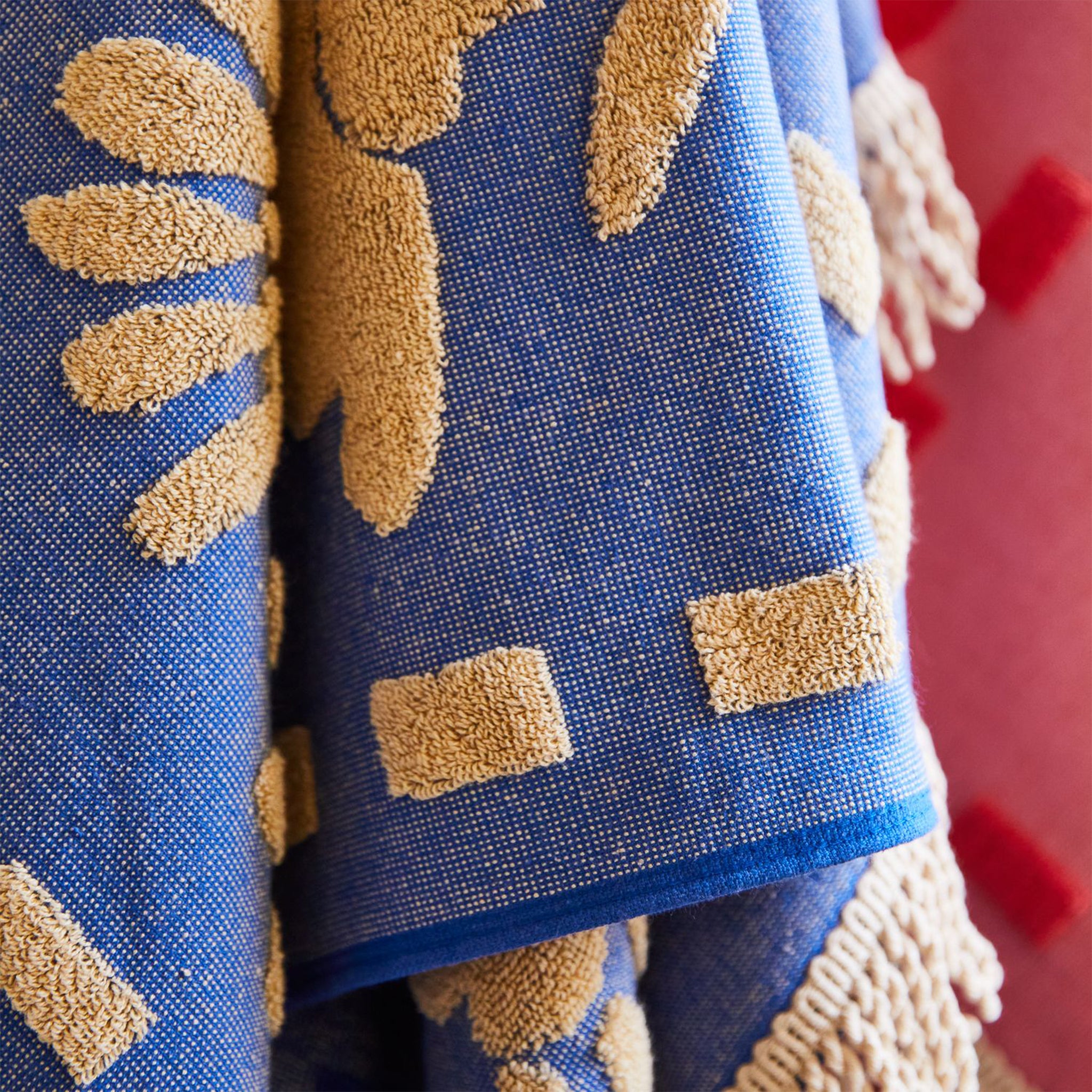 A blue and cream floral pattern bath towel with fringe detailing on two ends. 