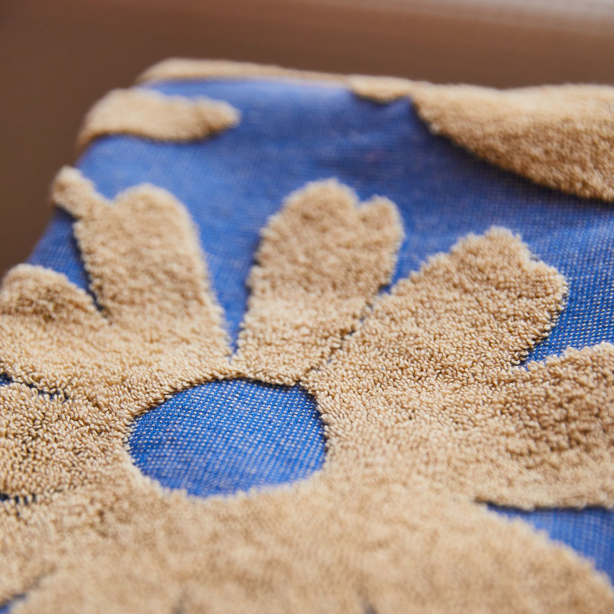 A blue hand towel with a cream floral print design and fringe details on each end. 