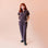 A model standing in front of a bookcase with a chocolate brown utility jumpsuit on with a zipper going up the front, a collar and a cinched waist.