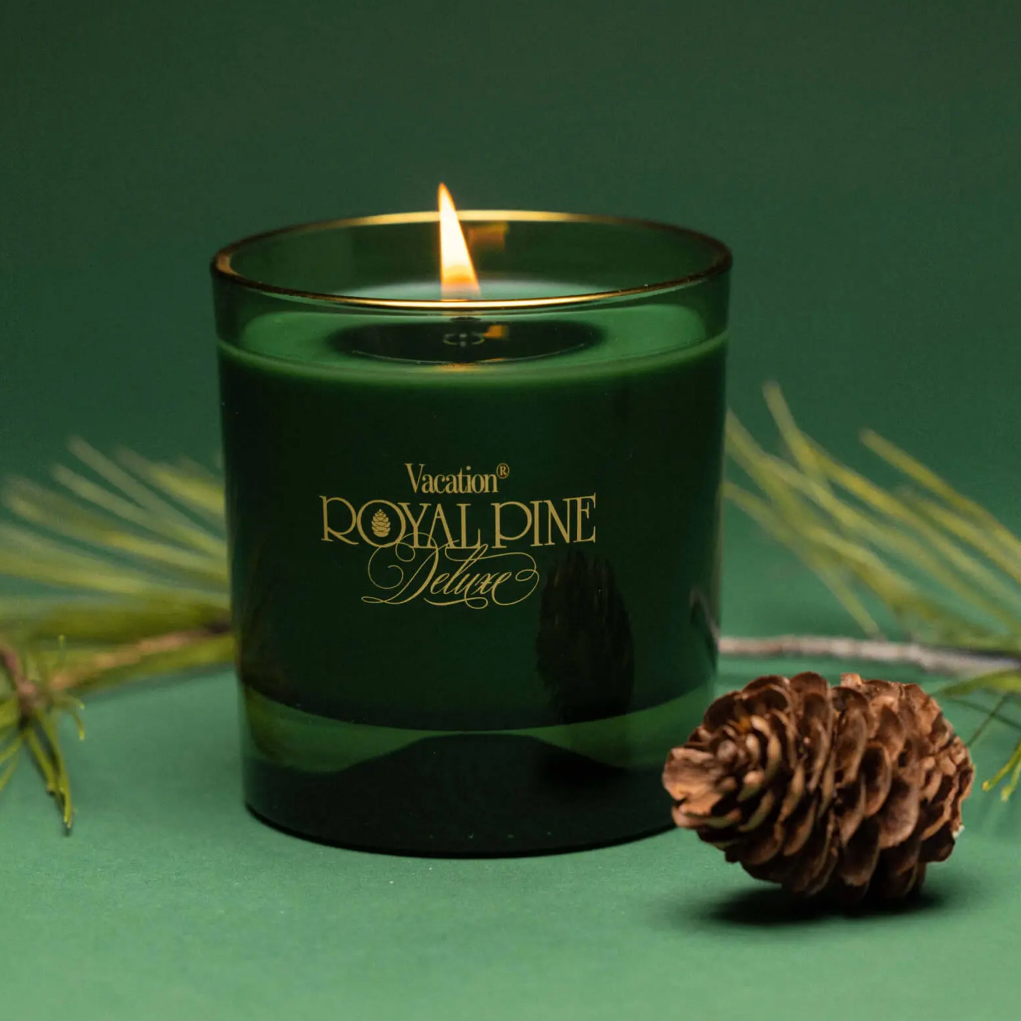 A green glass candle with with gold text that reads, &#39;Vacation Royal Pine Deluxe&#39;. 