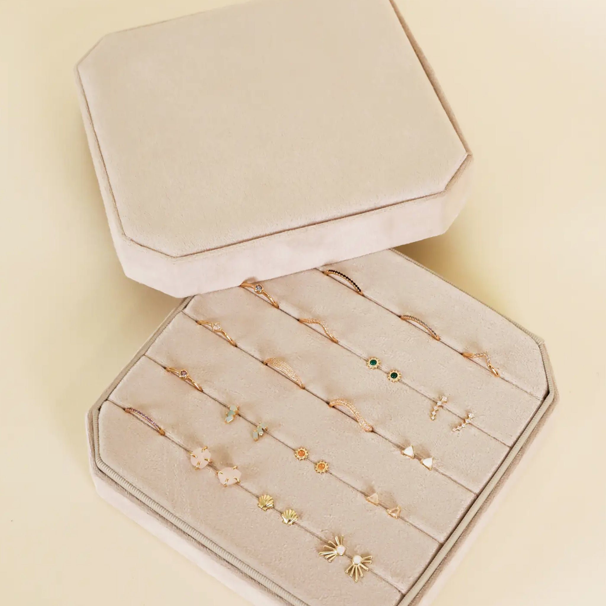 A cream velvet square jewelry box with slots for earrings and rings. 