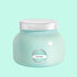 On a blue background is an aqua blue glass jar candle with a silver lid on top