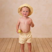 A yellow pair of boardshorts for kids with a textured wave pattern. 