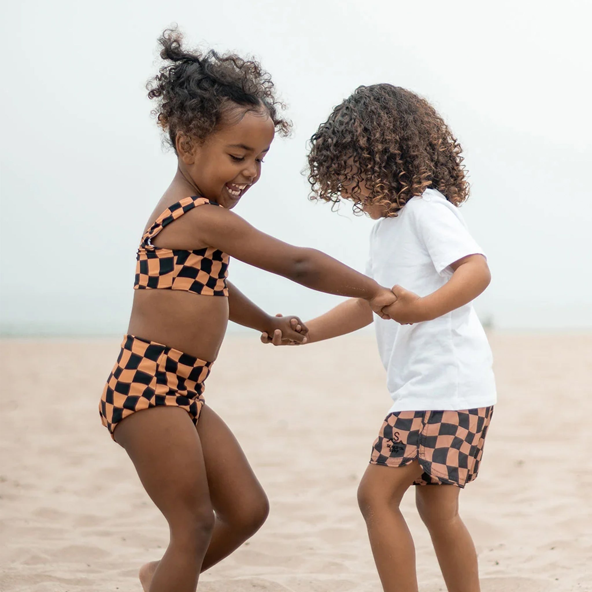 A brown and black wavy checkered print patterned boardshort along with a model wearing the wavy checkered two piece set. 