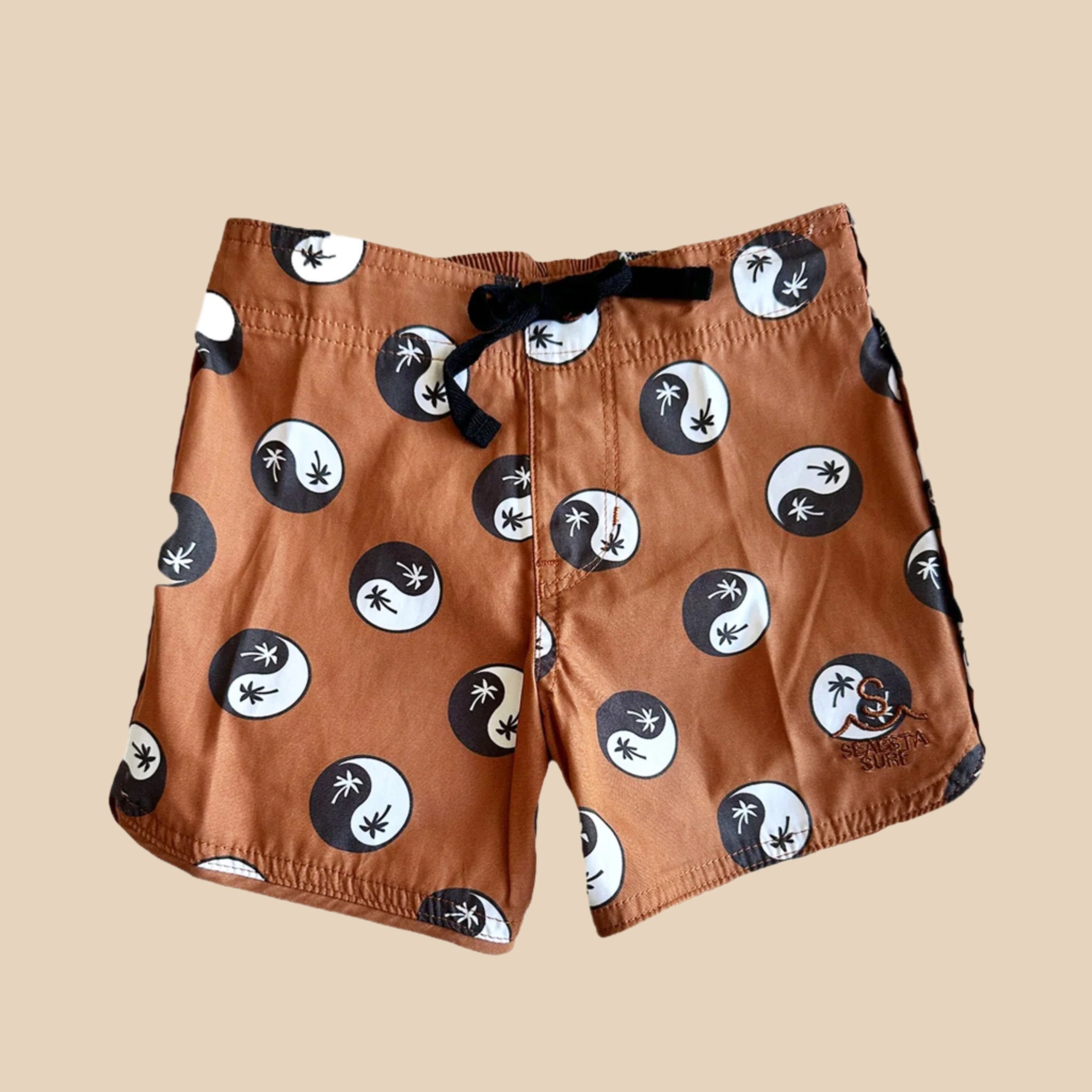 A burnt orange pair of boardshorts with a black and white palm tree yin yang print. 