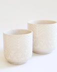 a smaller cream colored pot with chevron detail and speckles sits in front of a larger version of the same pot
