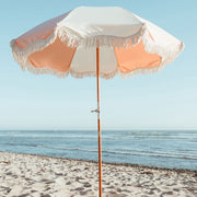 A pink and white paneled beach umbrella with an adjustable pole and white fringe detailing around the edge of the shade.