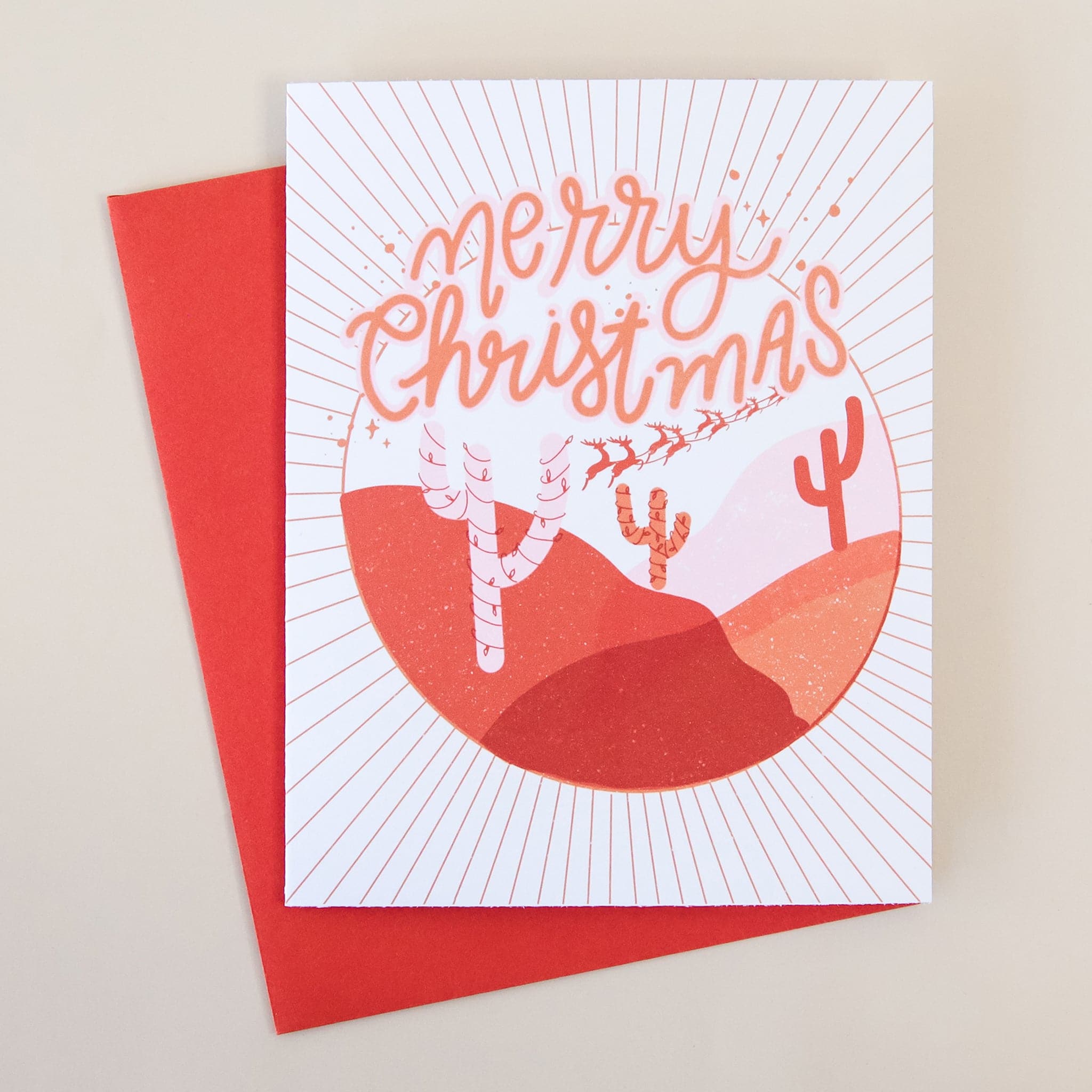 A white card with a red desert scape graphic with cacti and text that reads, "Merry Christmas" at the top of the design.