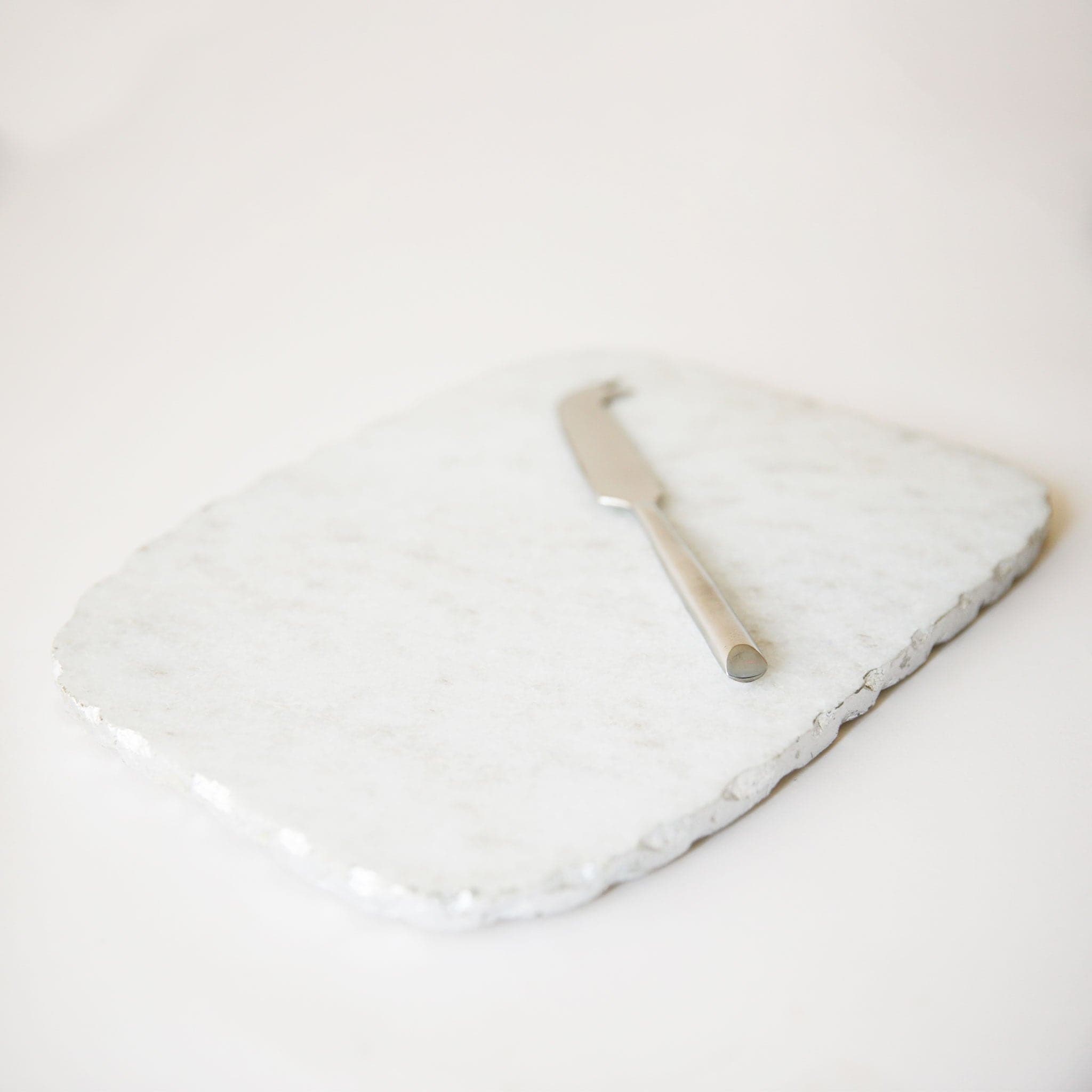 On a white background is a white marble cheese board with a cutting knife and a silver edge.