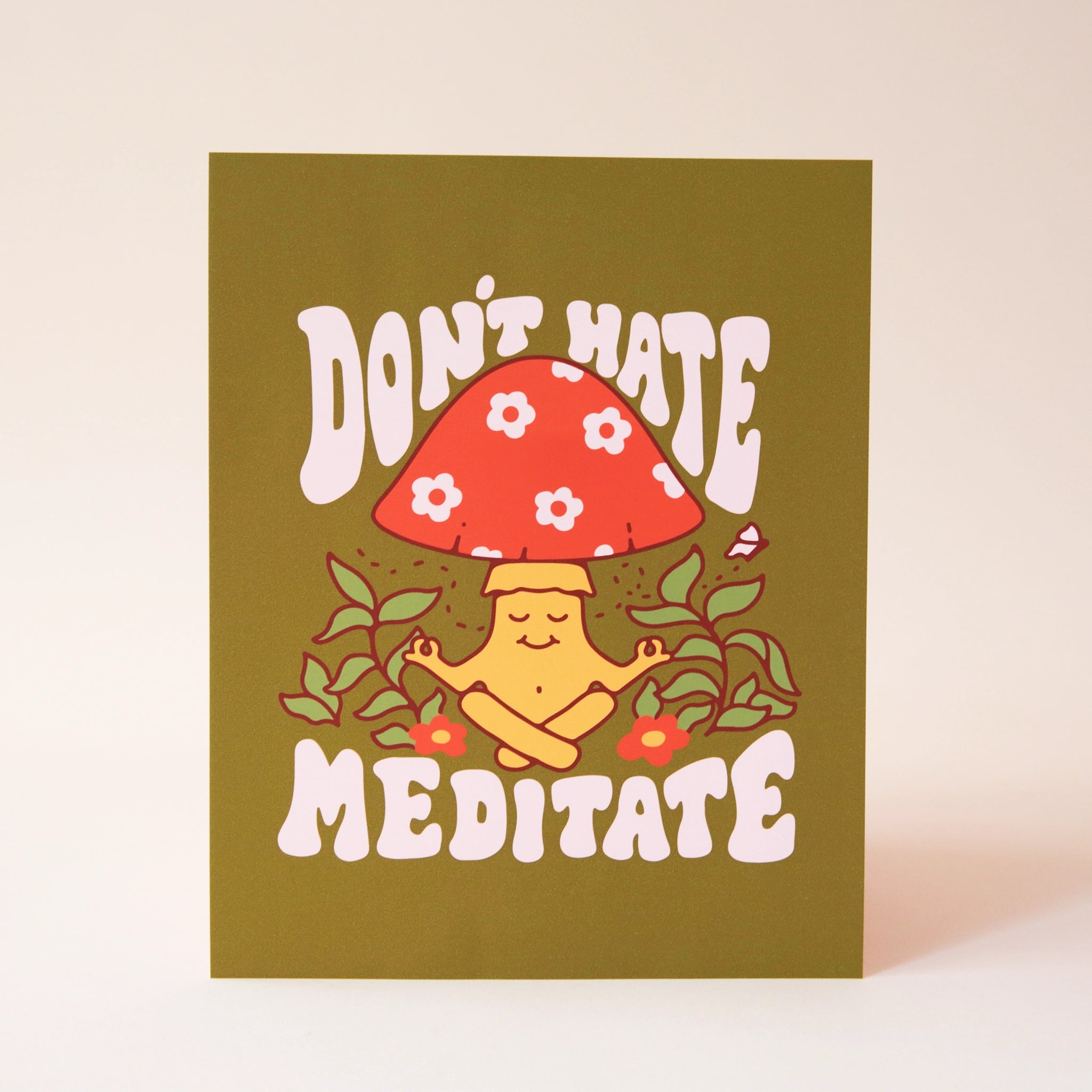 An olive green art print with a mediating mushroom graphic with a red and daisy printed top and a smiling face along with white text above and below the graphic that reads, "Don't Hate Meditate".