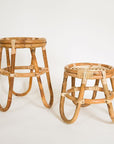 In front of a white background is tow rattan plant stands. They both have three curved legs and a round top. The plant stand on the left is taller than the one on the right.