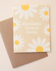 A tan card with white and yellow daisies all over the edges along with groovy text in the center that reads, "Welcome Little Babe" along with a Kraft brown envelope.