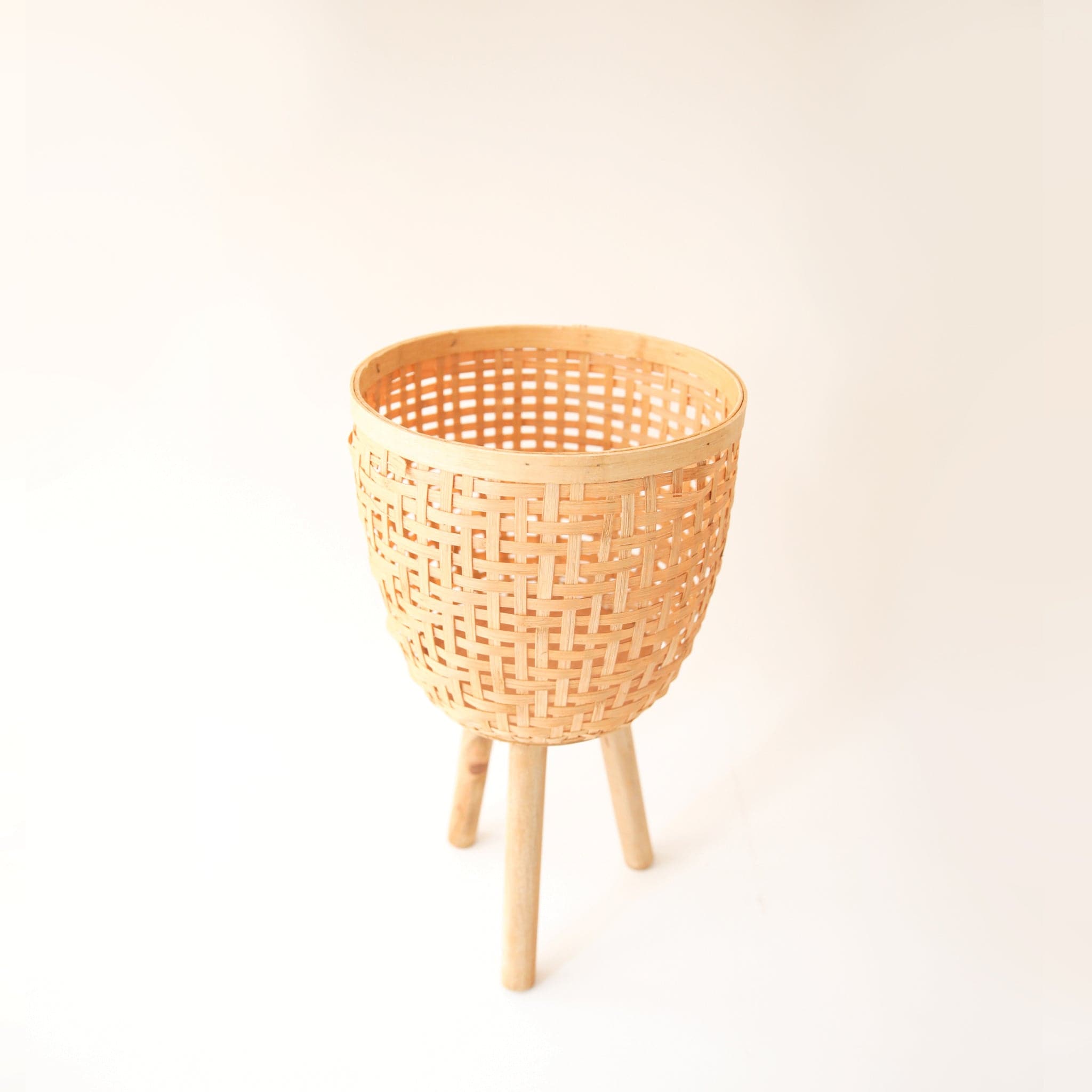 Three different sized, light colored rattan basket plant holders, each standing on three wooden legs. Each basket sold separately.