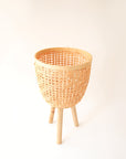 Three different sized, light colored rattan basket plant holders, each standing on three wooden legs. Each basket sold separately.