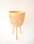 Three different sized, light colored rattan basket plant holders, each standing on three wooden legs. Each basket sold separately.