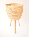 Three different sized, light colored rattan basket plant holders, each standing on three wooden legs. Each basket sold separately.