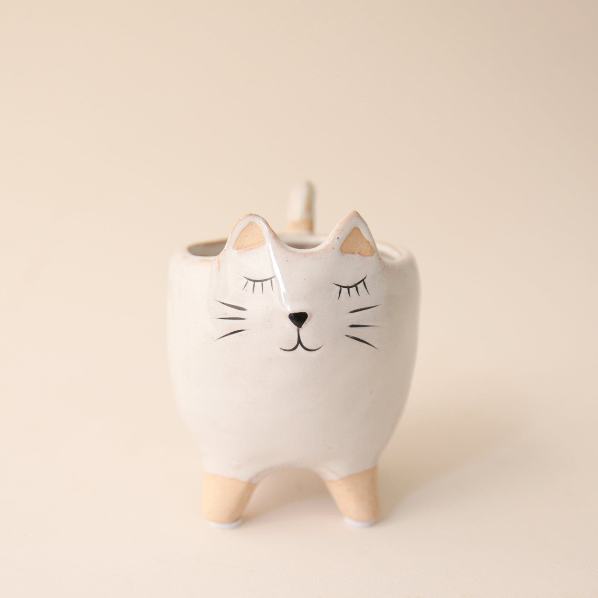 a small white planter shaped as a cat with a painted cat face.,