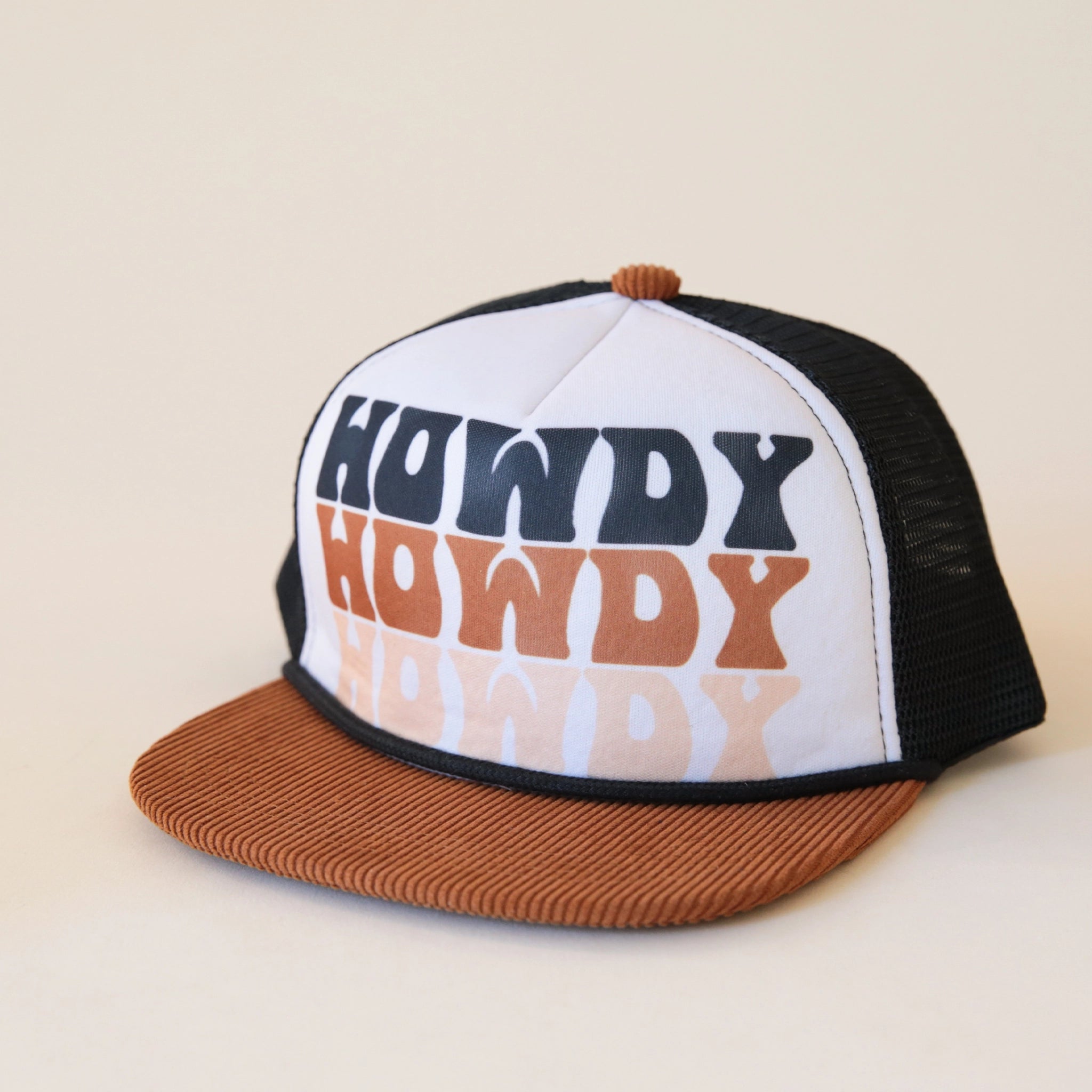 A children trucker hat with a white panel, black mesh backing and a brown corduroy bill along with text that reads, "Howdy Howdy Howdy" stacked vertically on top of one another in a black, brown, and cream colored letters.