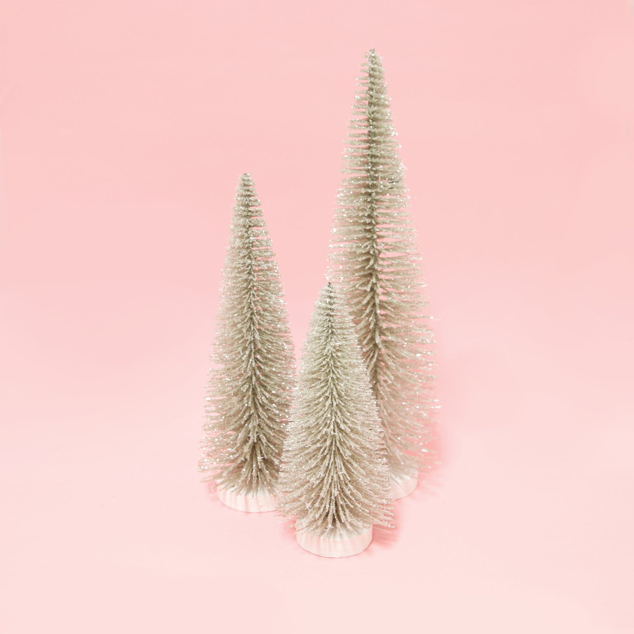 three silver bristle tress of varying heights on a pink background