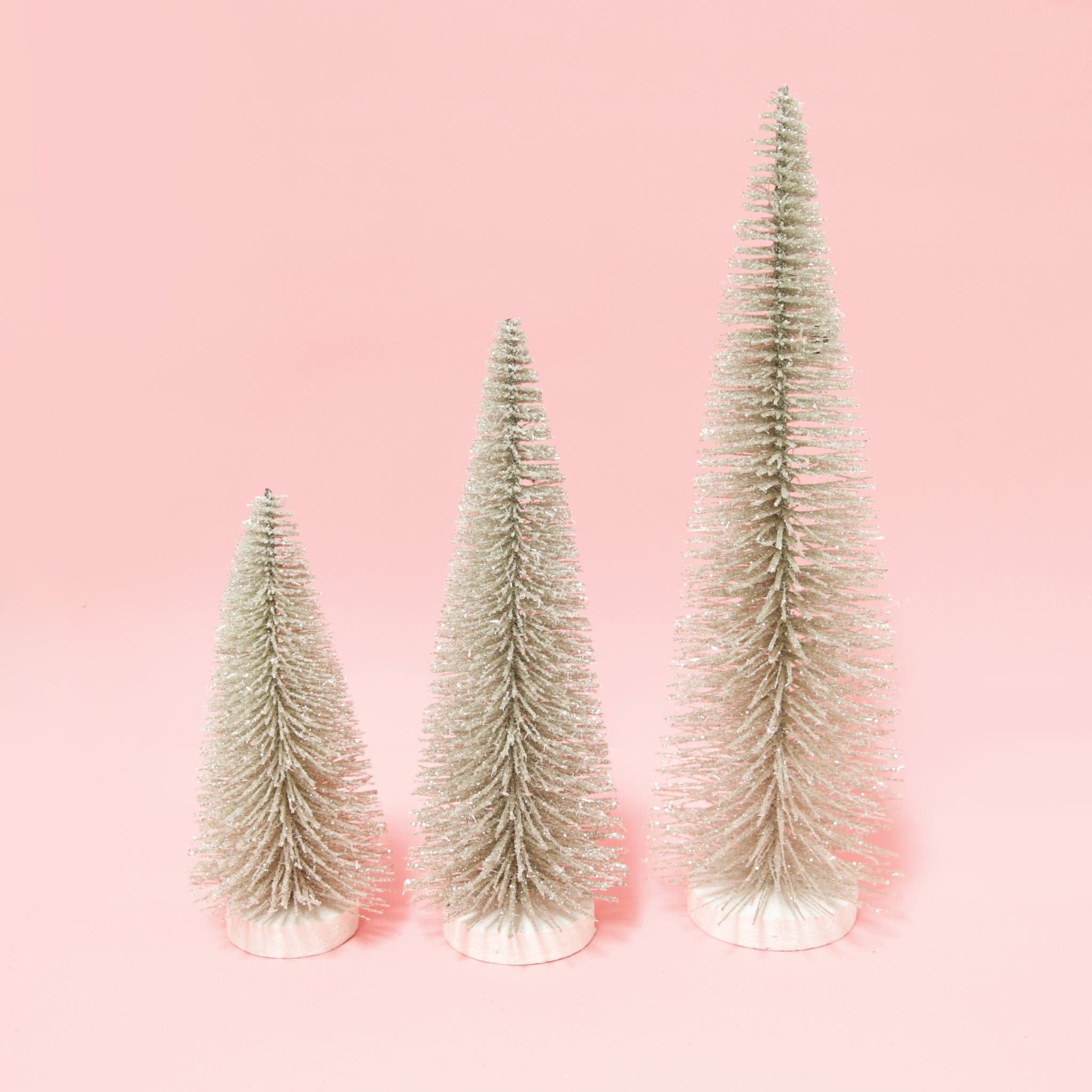 three silver bristle tress of varying heights on a pink background