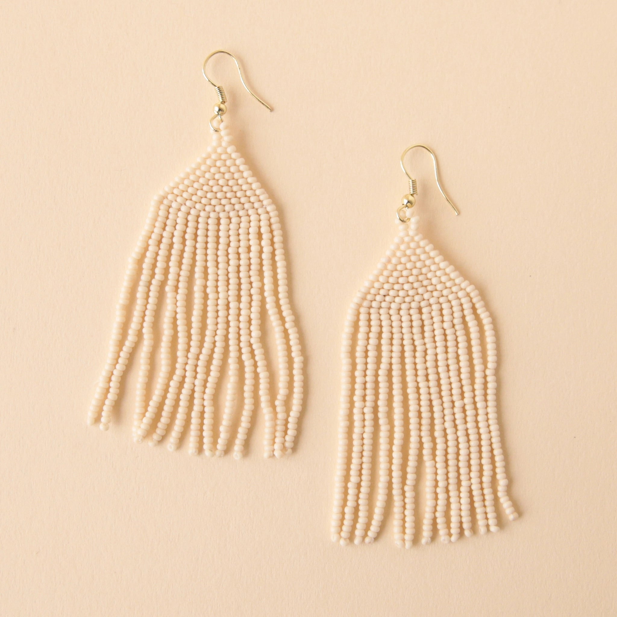 A gold plated hook earring attached to a triangle shaped glass beaded earring in a cream shade along with a fringe detail on the bottom edge.