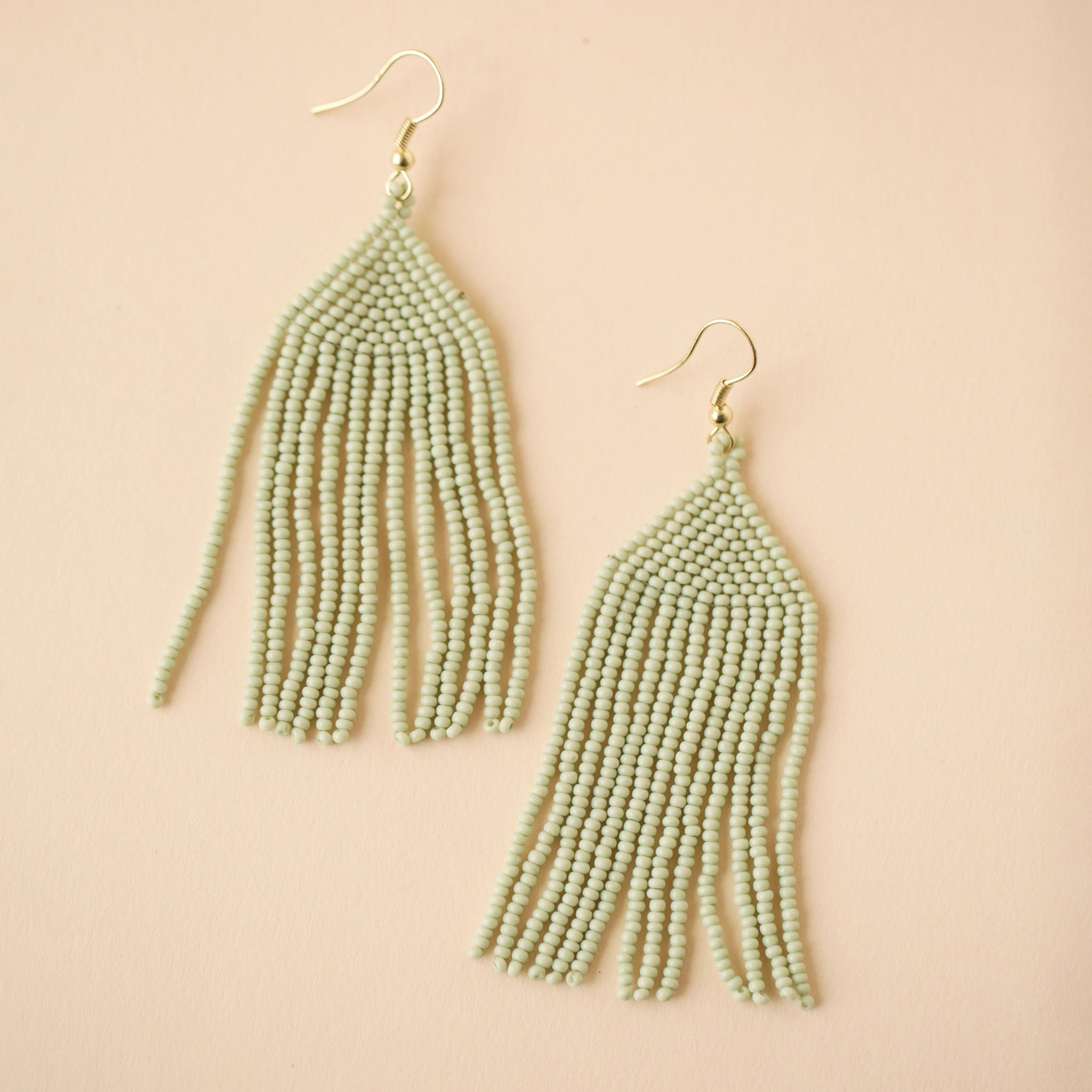 A gold plated hook earring attached to a triangle shaped glass beaded earring in a mint green shade along with a fringe detail on the bottom edge.