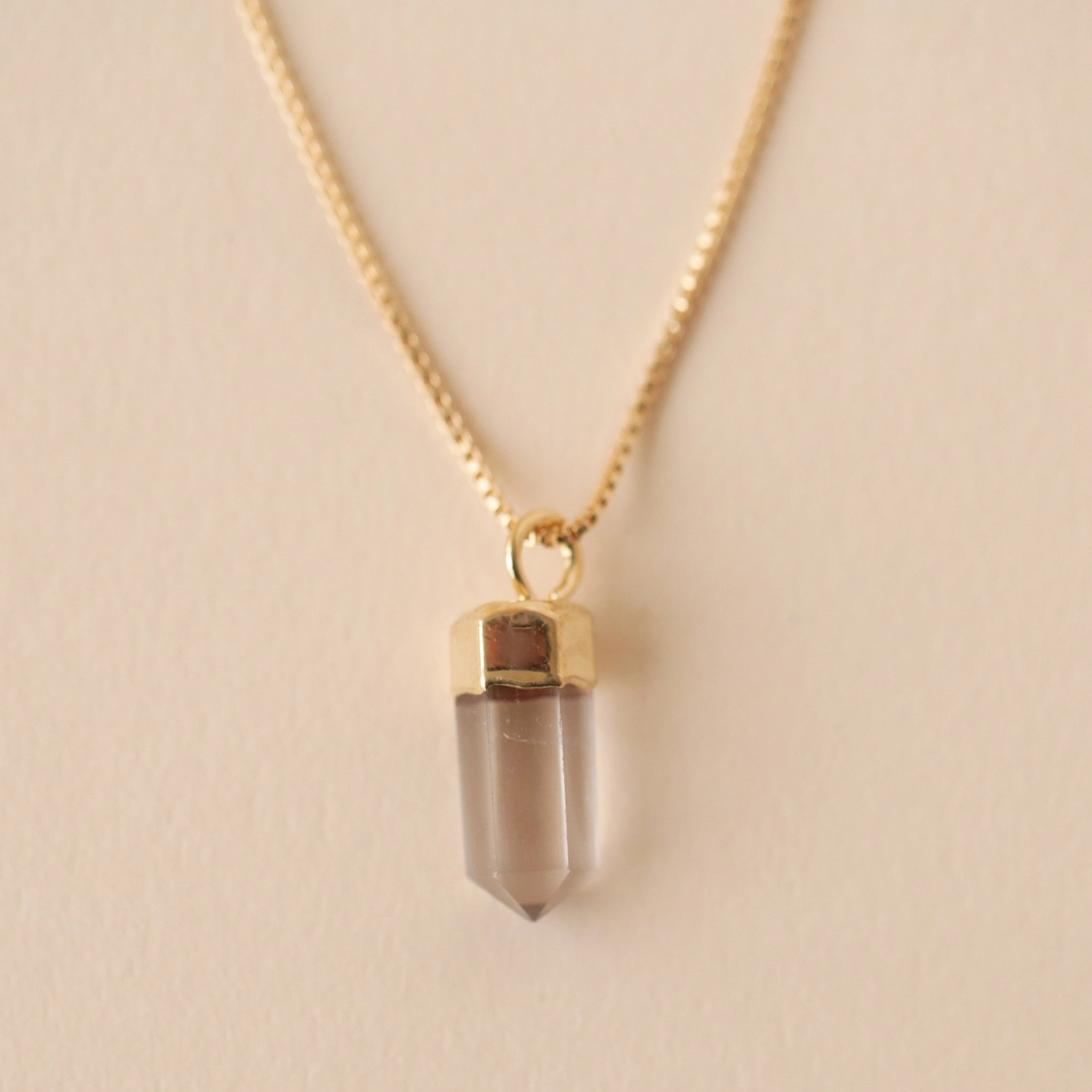 A dainty gold chain necklace with a clear quartz crystal point pendant.