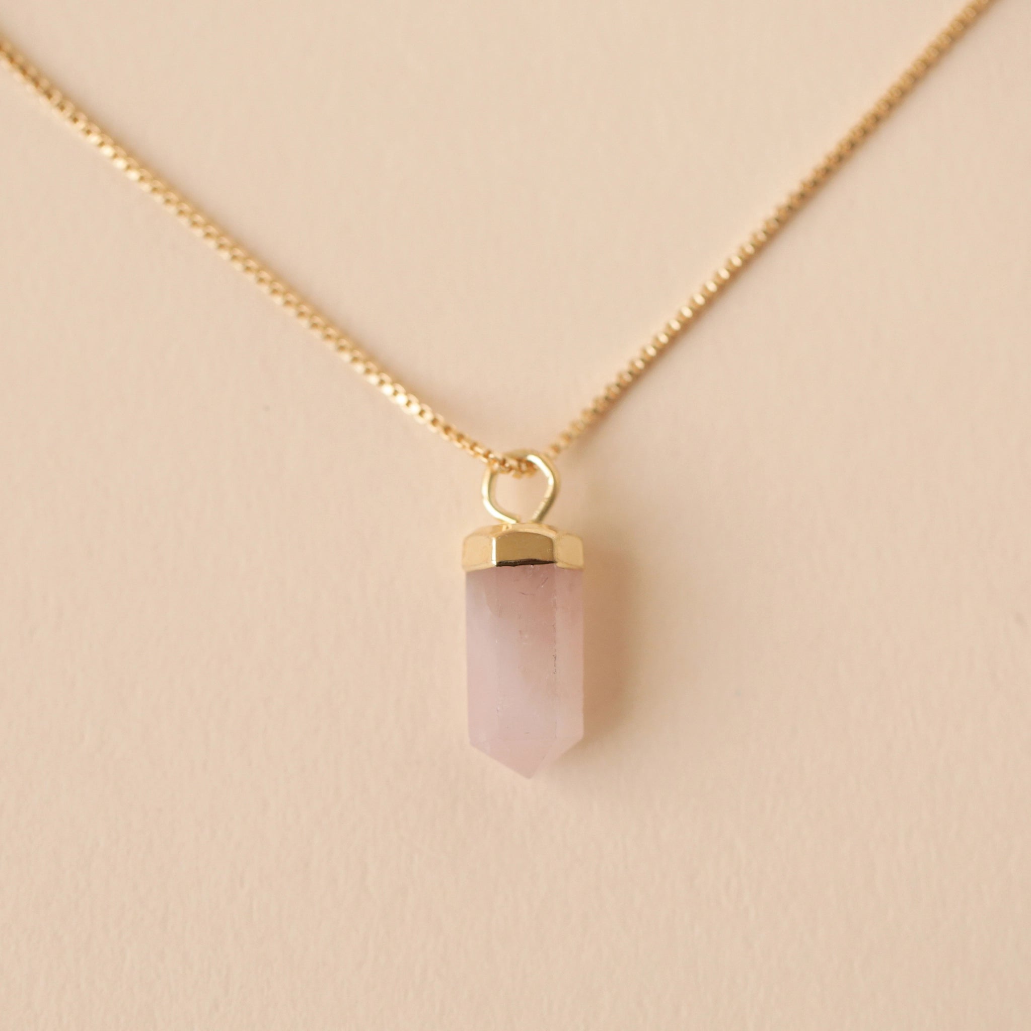 A dainty gold chain necklace with a rose quartz crystal point pendant with an extender for added length and a smaller rose quartz crystal on the back where the clasp is.