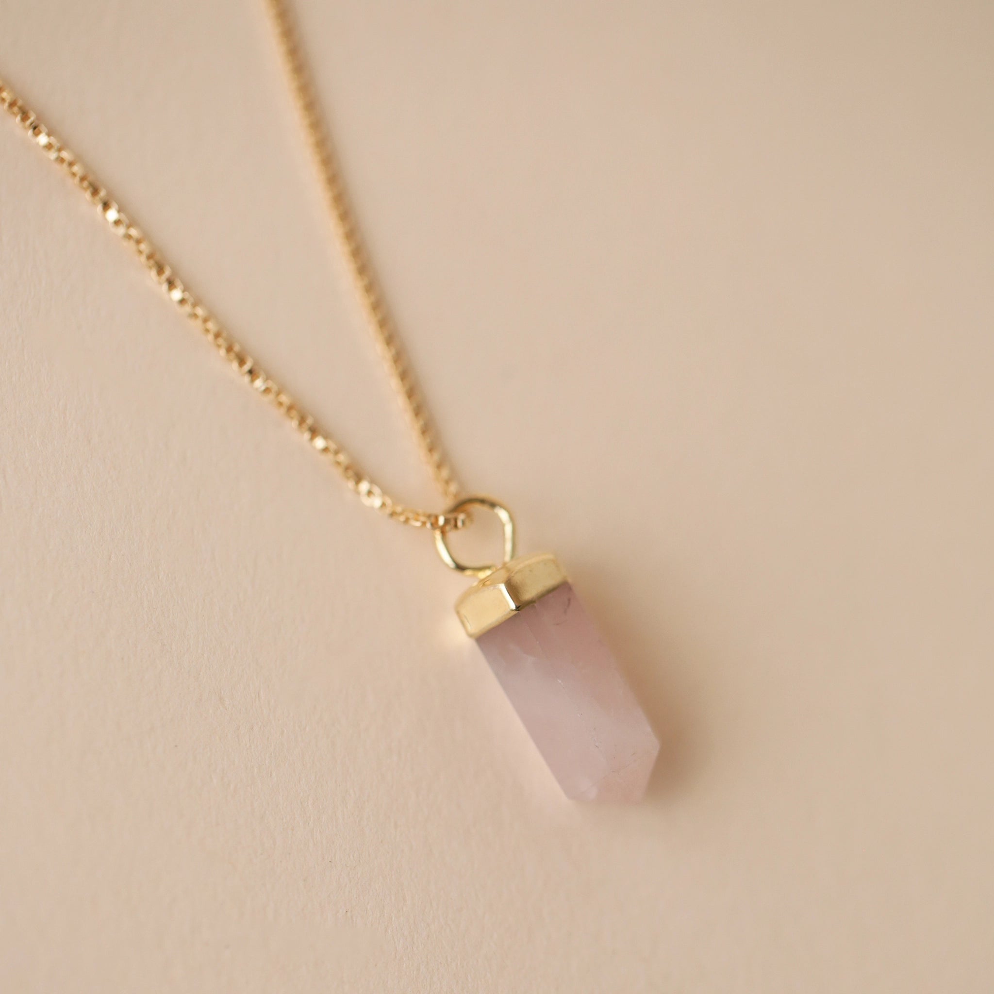 A dainty gold chain necklace with a rose quartz crystal point pendant with an extender for added length and a smaller rose quartz crystal on the back where the clasp is.