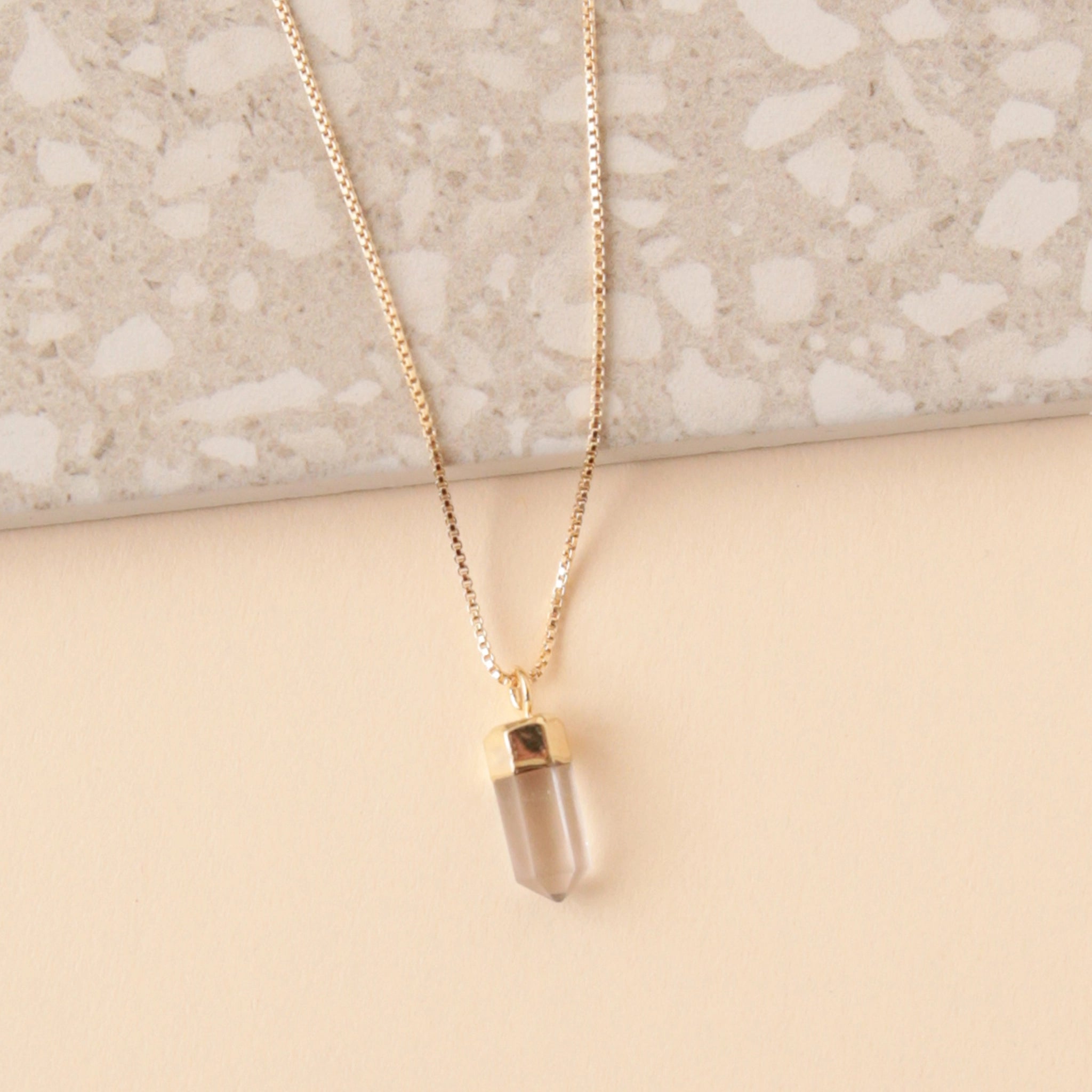 A dainty gold chain necklace with a clear quartz crystal point pendant.