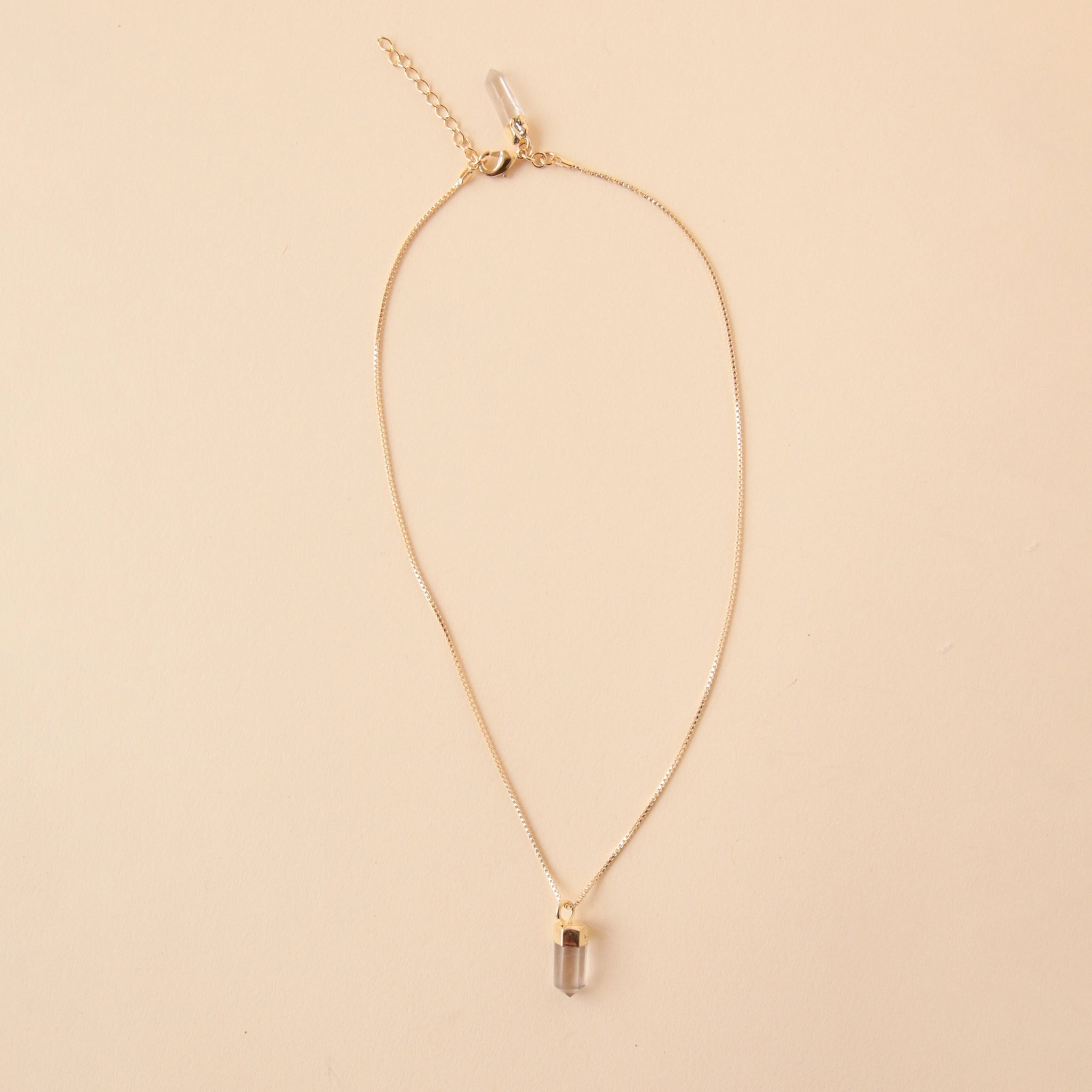 A dainty gold chain necklace with a clear quartz crystal point pendant.