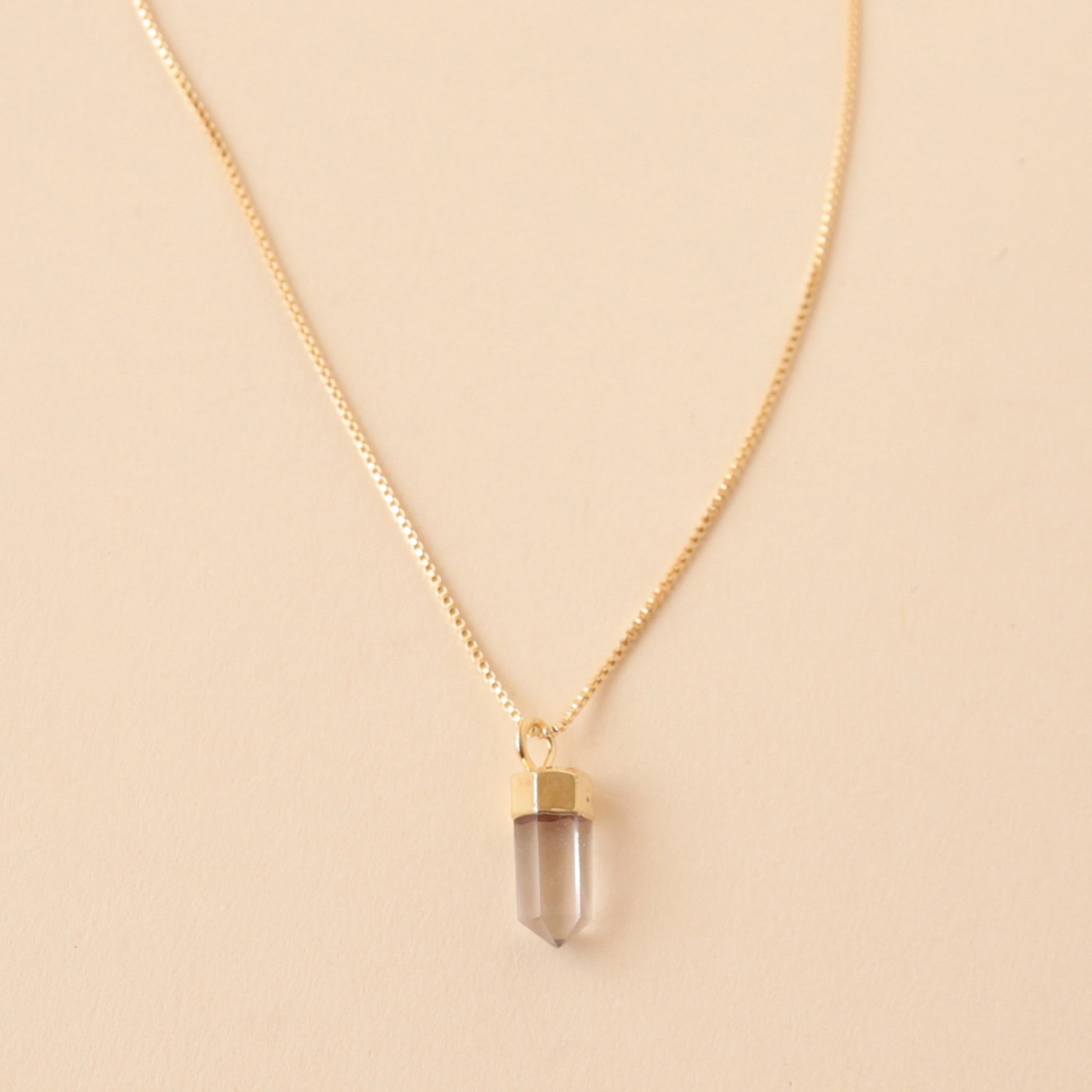 A dainty gold chain necklace with a clear quartz crystal point pendant.