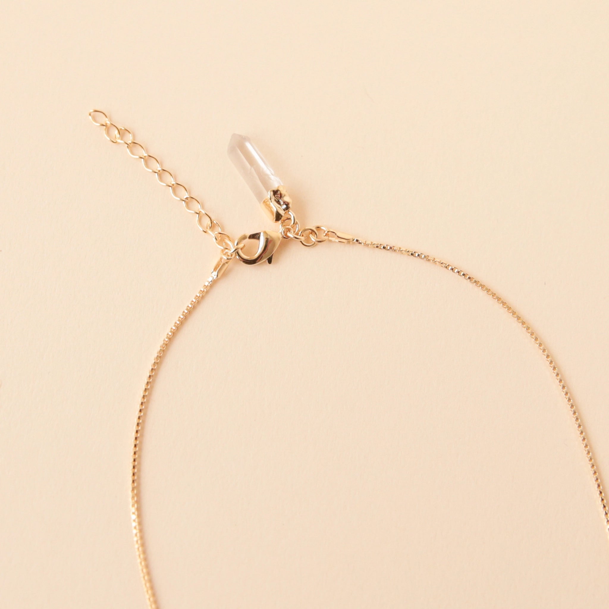 A dainty gold chain necklace with a clear quartz crystal point pendant with an extender for added length and a smaller clear quartz crystal on the back where the clasp is.