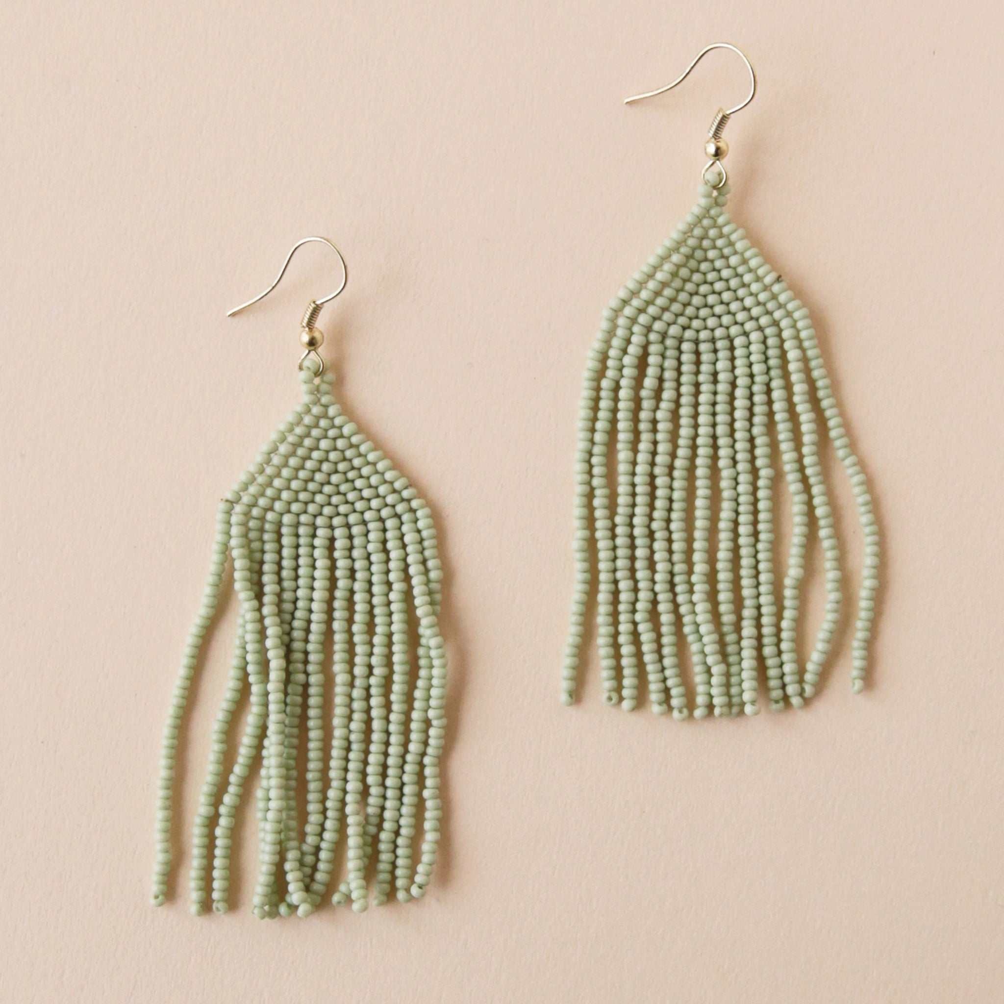 A gold plated hook earring attached to a triangle shaped glass beaded earring in a mint green shade along with a fringe detail on the bottom edge.