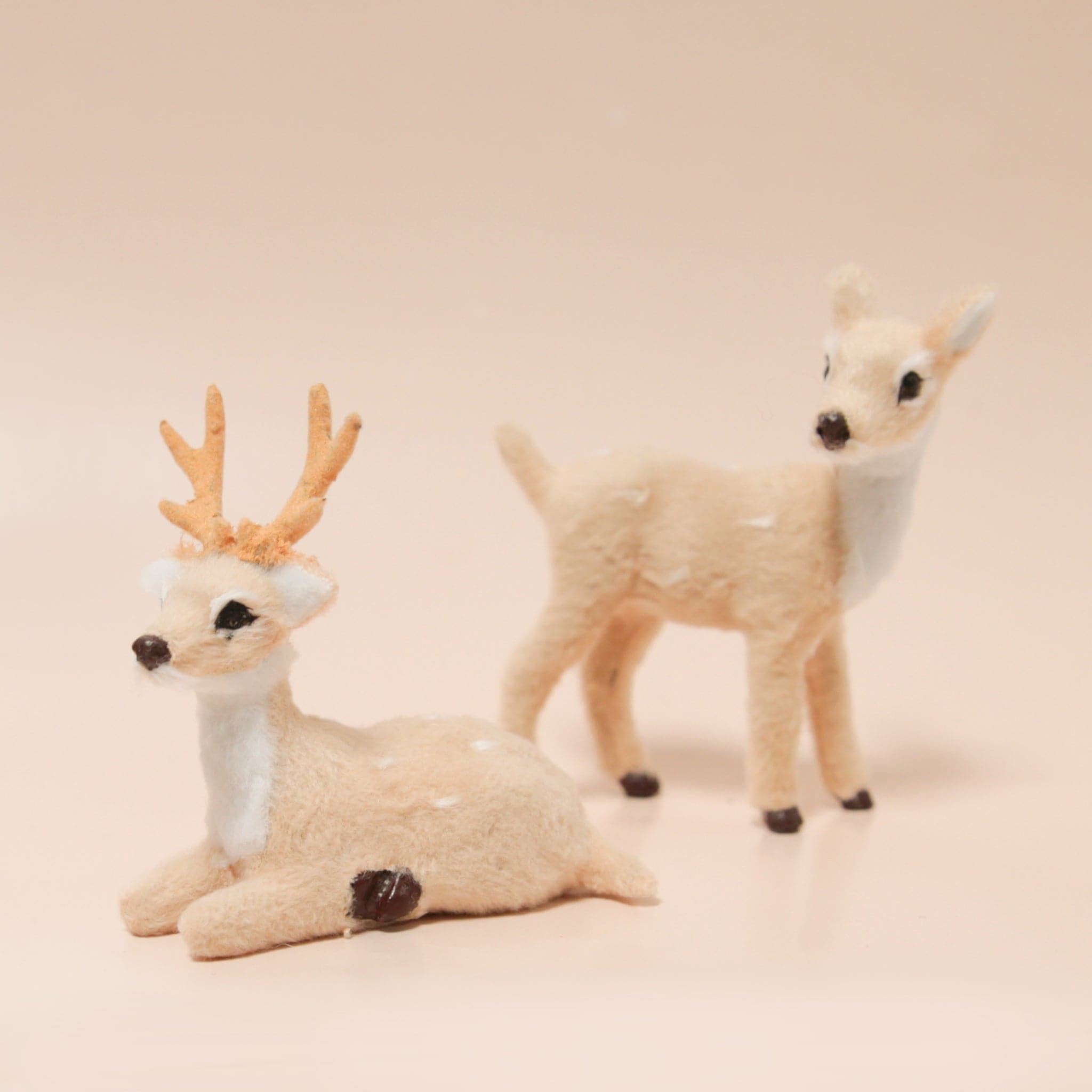 Two flocked cream colored reindeer figures rest atop a light peach colored background