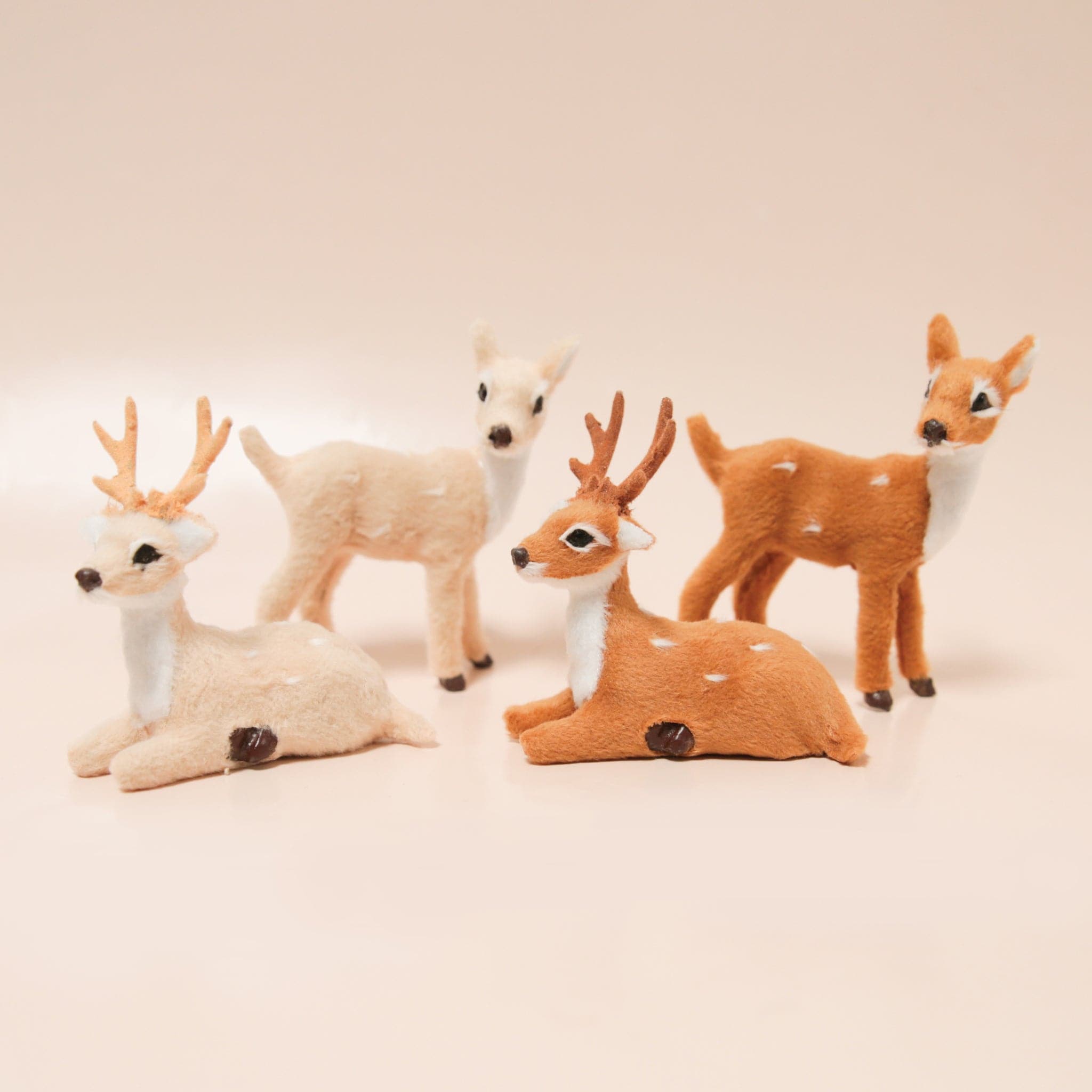 A variety of flocked reindeer figures in cream and brown rest on a light peach colored background.