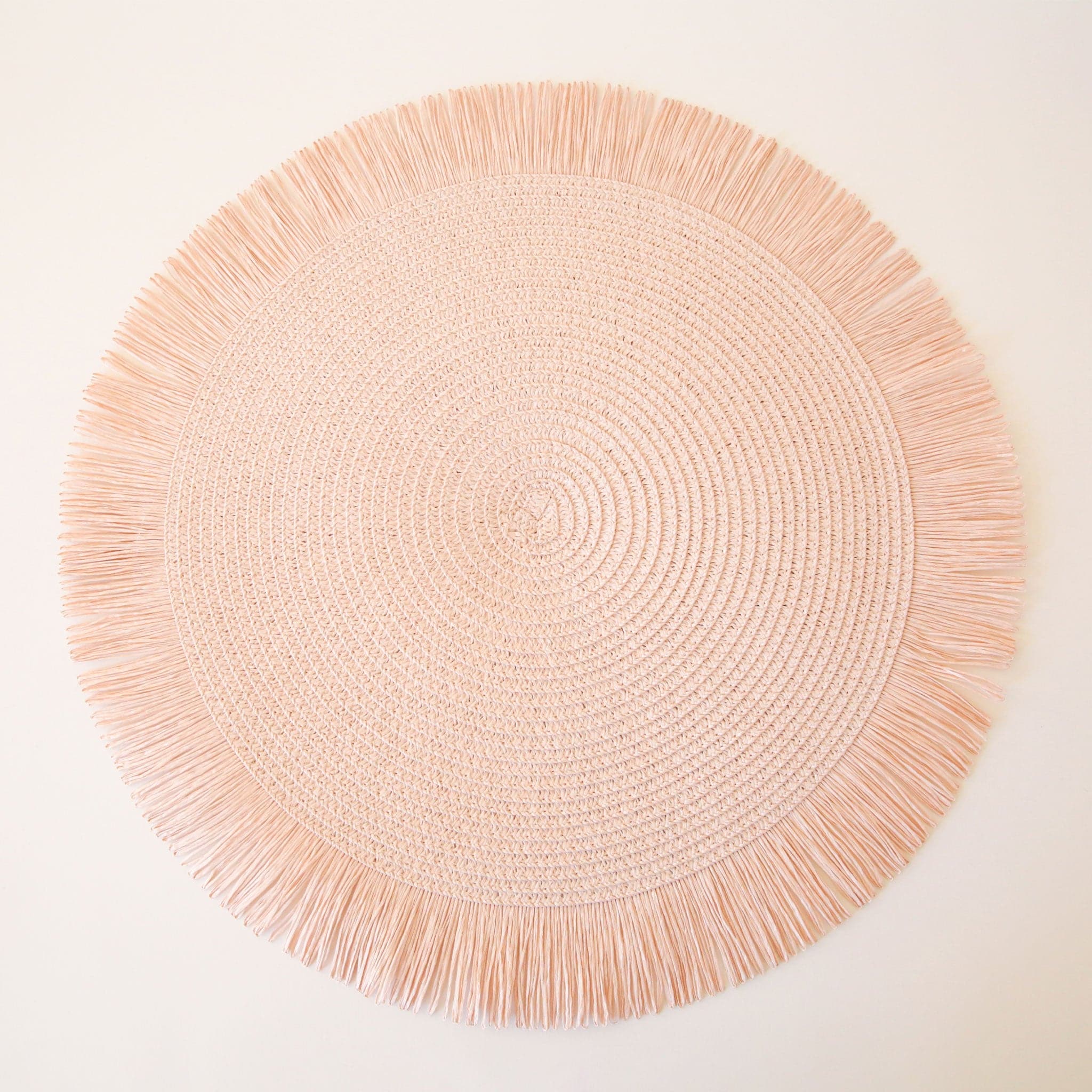 Textured, blush pink circle place mat with bordered in a soft pink fringe. 