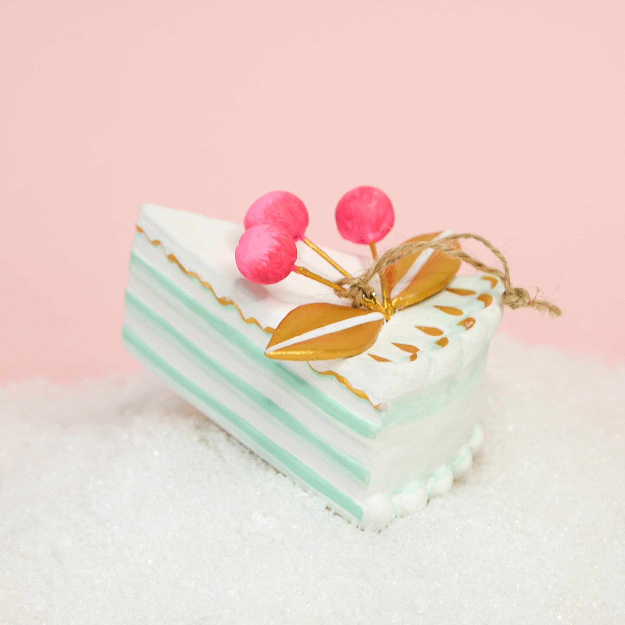 A piece of cake ornament with mint green layers and pink berries on top.