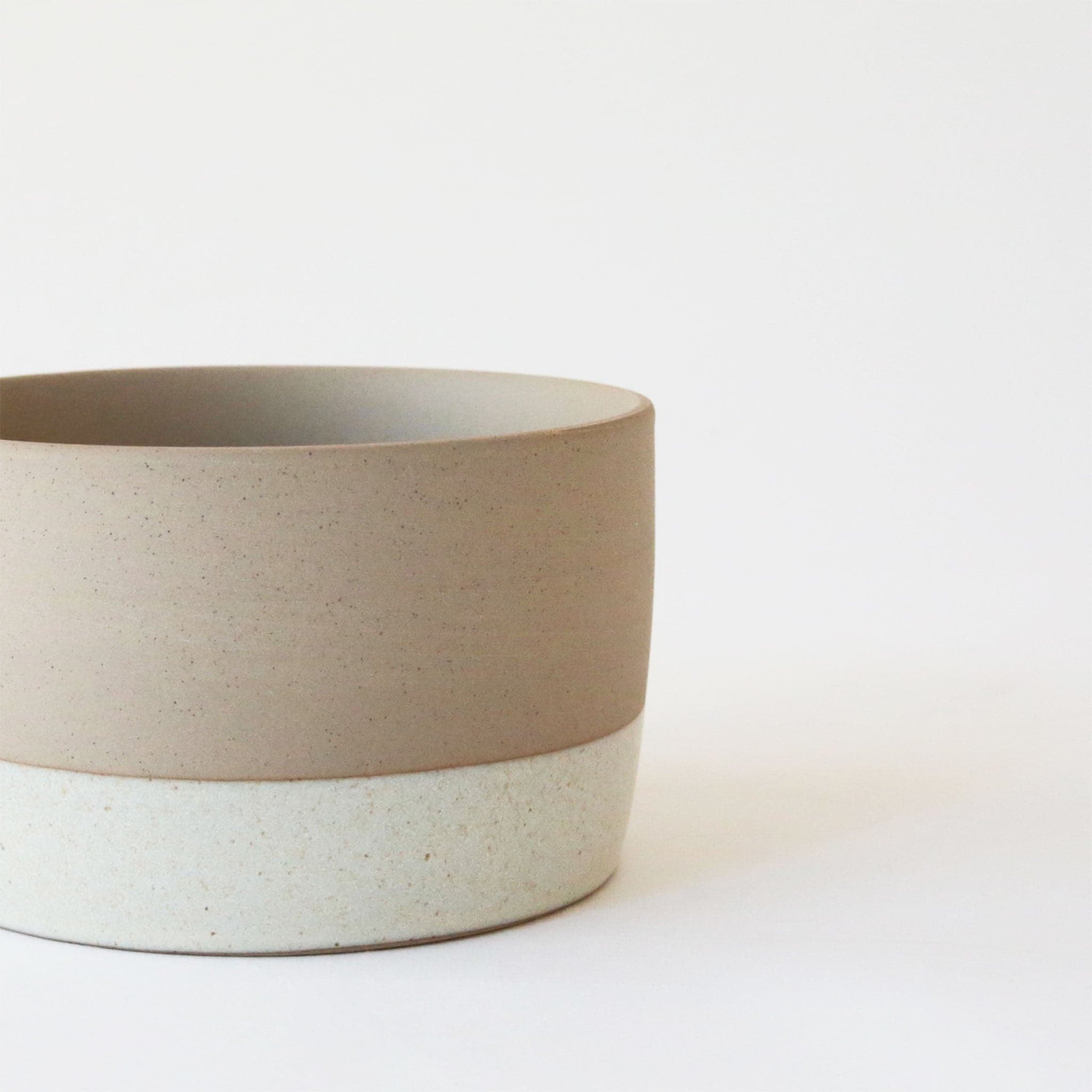 A two-toned ceramic pot with tiny black speckles. The top half is a creamy beige and the bottom is white.