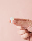 On a pink background is a model holding a tiny opal stone in the shape of a mushroom. 