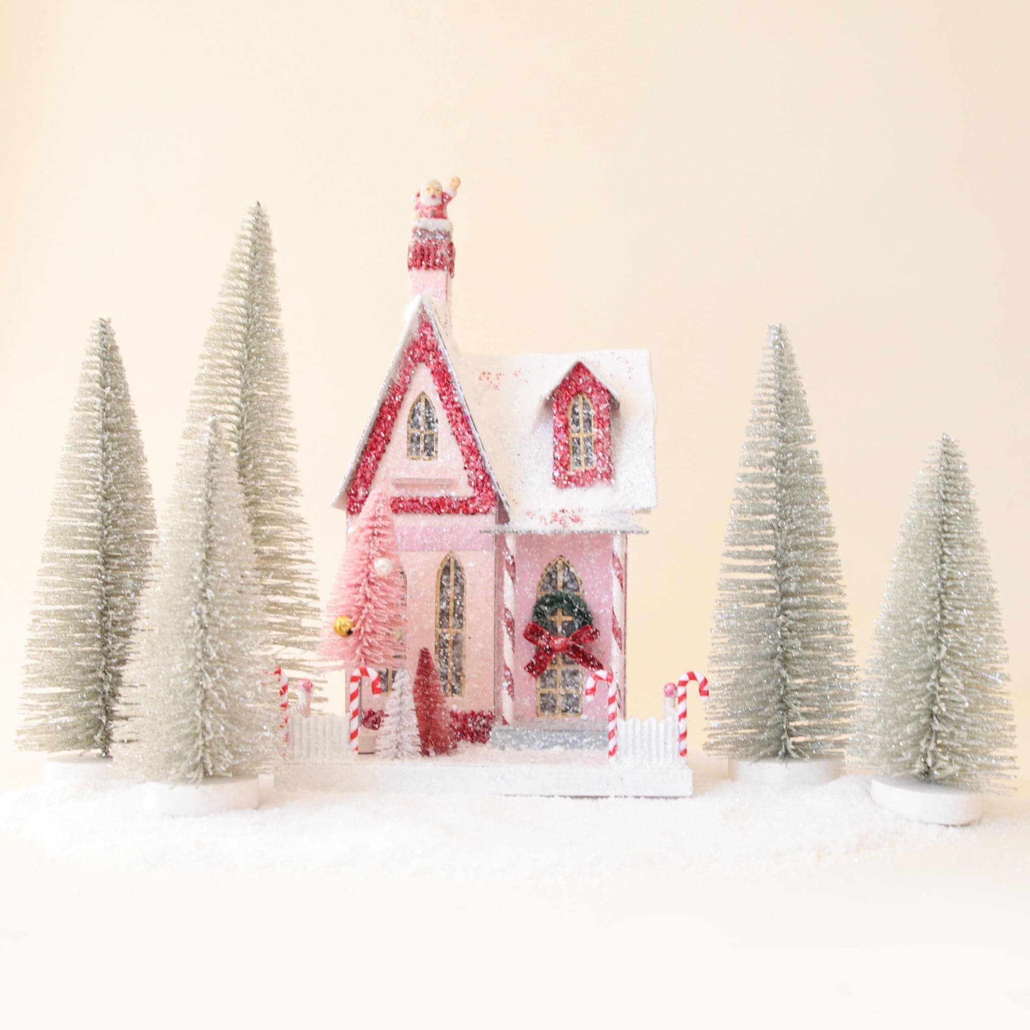 a pink and white holiday house surrounded by silver bristle tress on a ground of snow