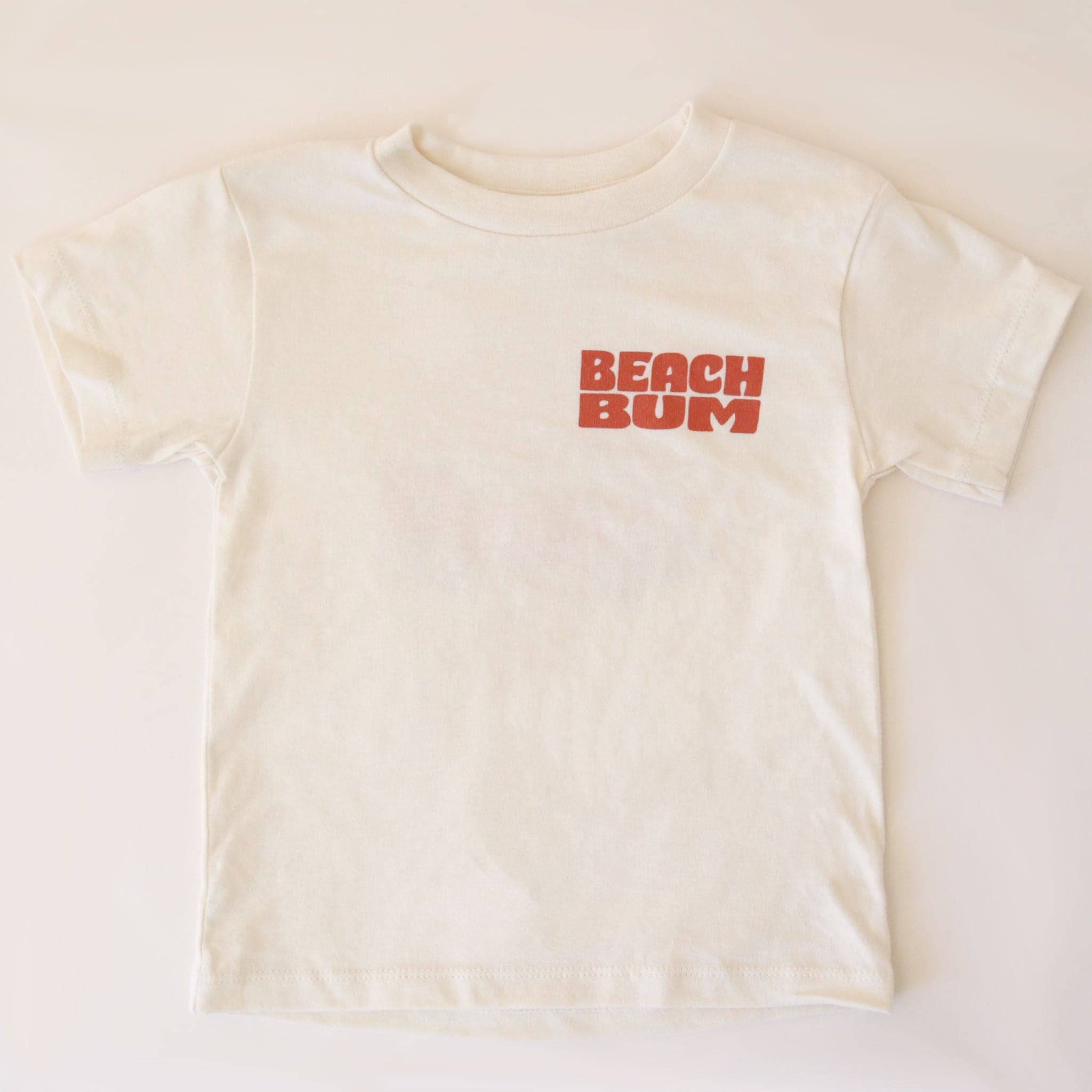 The front of the cream colored t-shirt that features text in the top right hand corner of the shirt that reads, &quot;Beach Bum&quot; in burnt orange letters.