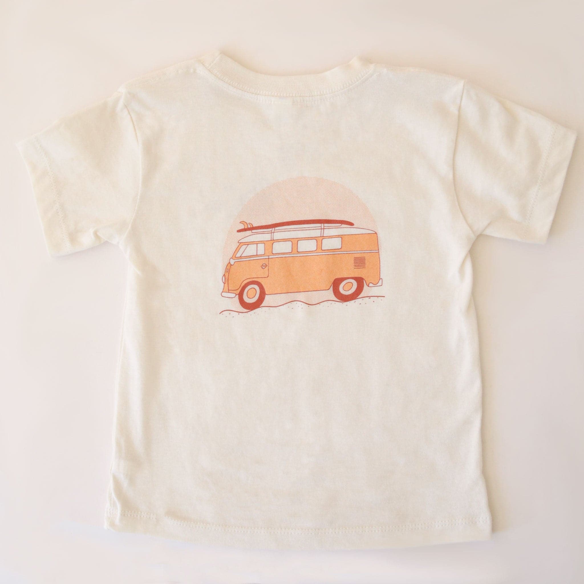 The back of the cream colored t-shirt that features a yellow VW bus graphic with a burnt orange surfboard on top.